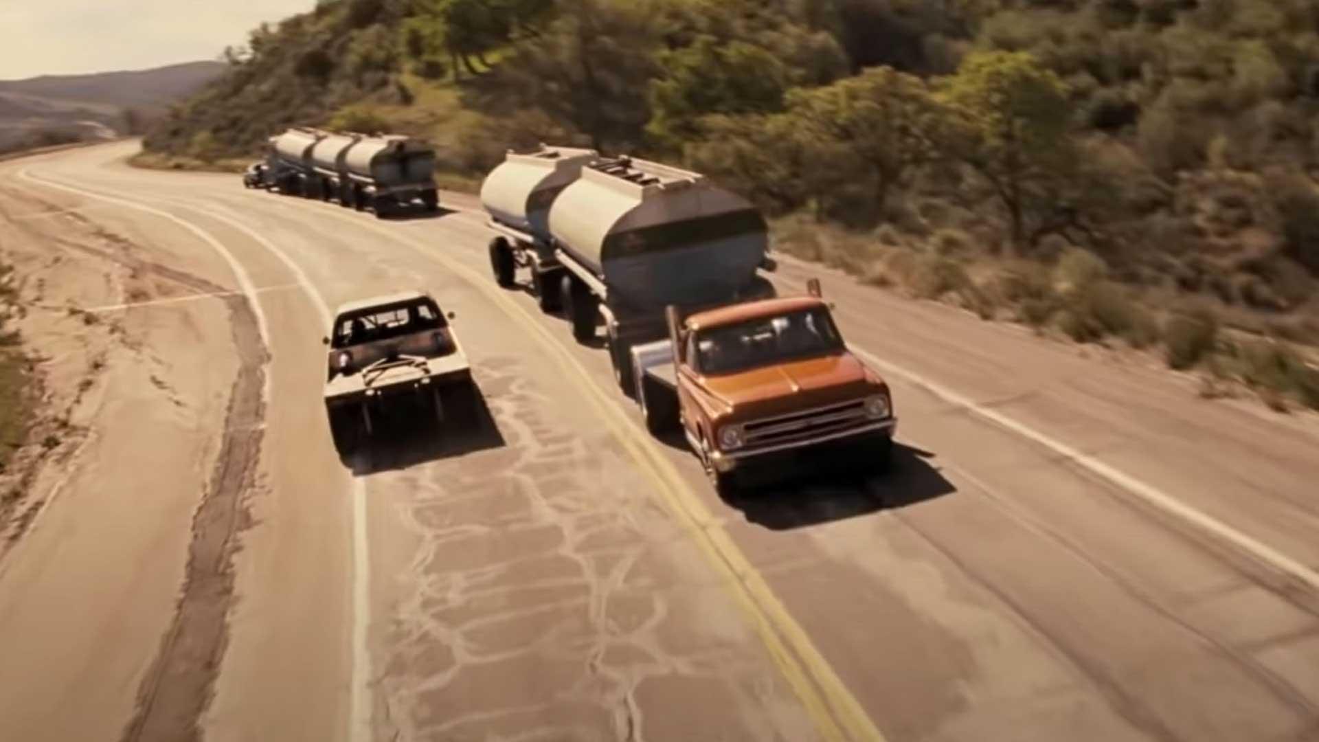Filmauto's uit Fast and Furious rijdend op een snelweg naast vrachtwagen