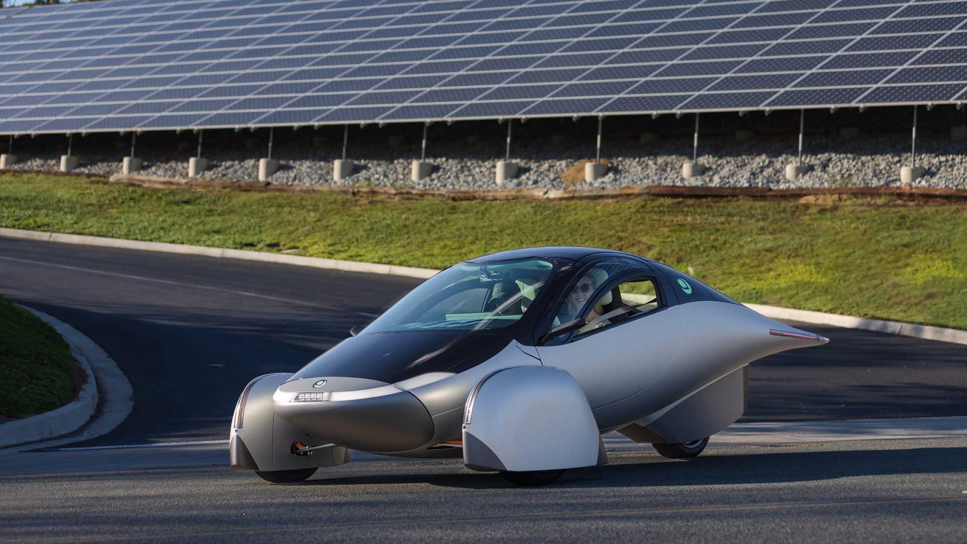 Aptera driewieler conceptversie rijdend op een weg schuin voor voor wat zonnepanelen