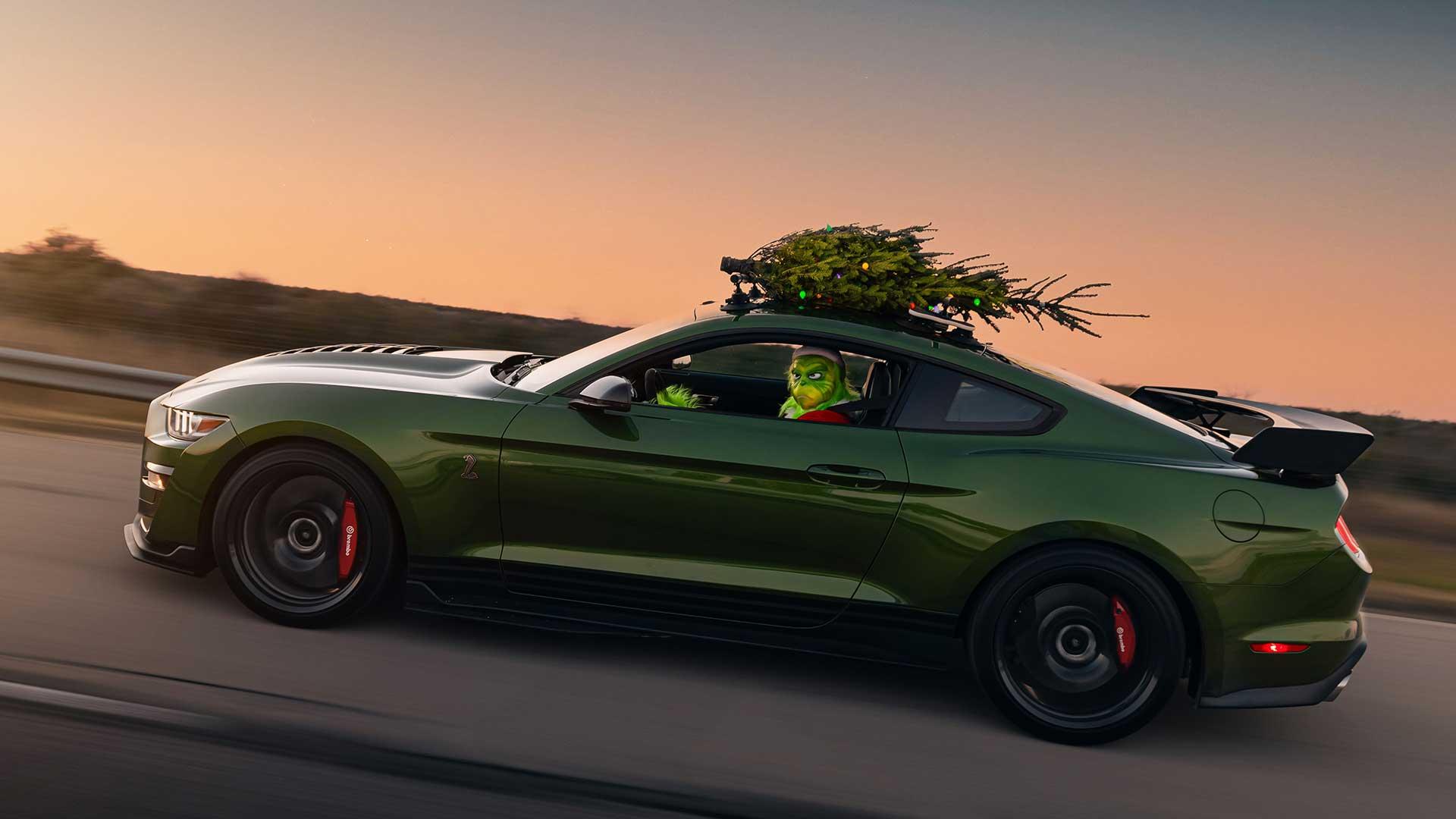 Ford Mustang Hennessey rijdend zijkant met een kerstboom op het dak en The Grinch achter het stuur