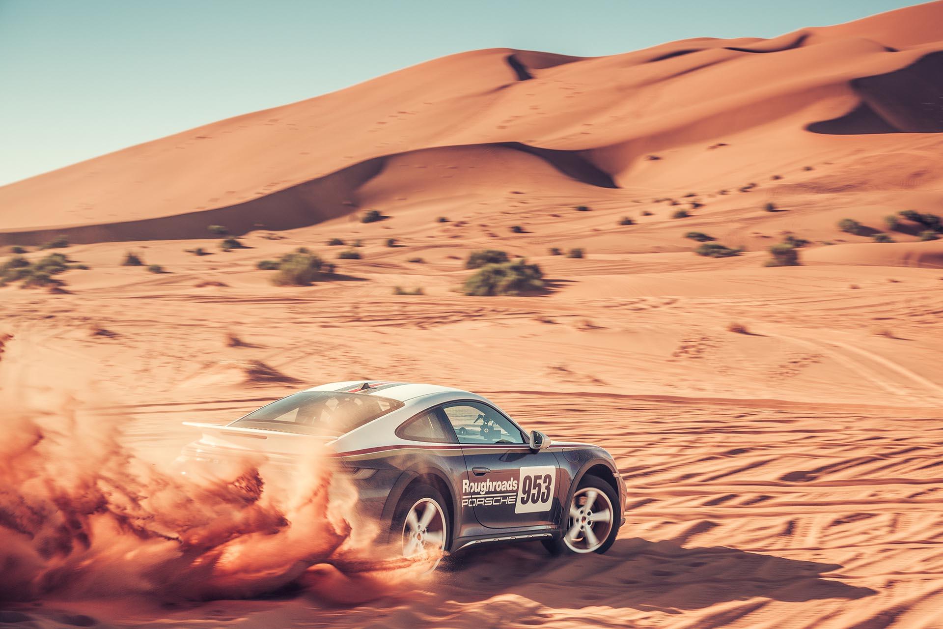 Porsche 911 Dakar rijdend op de weg in de woestijn schuin achter