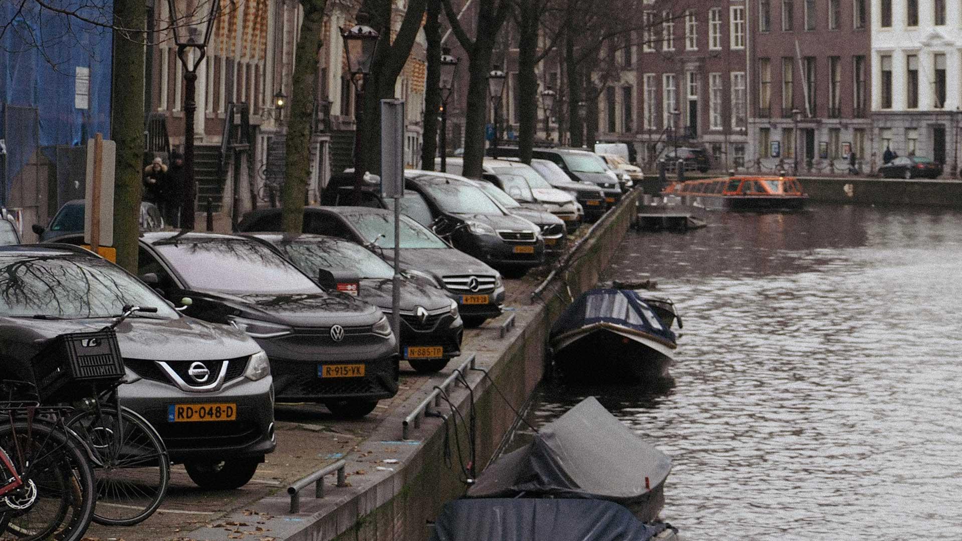 Auto's geparkeerd aan de gracht in Amsterdam (Unsplash)