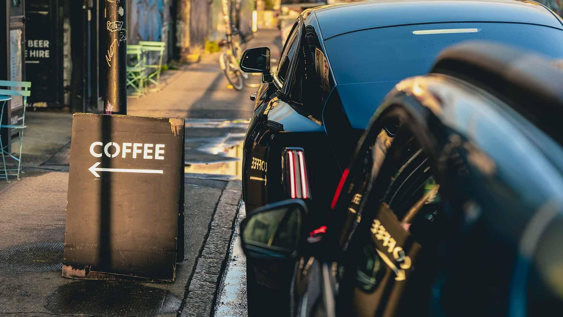 Rolls-Royce Spectre en Dacia Spring geparkeerd naast bord coffee koffie