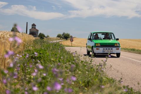 Renault 5 elektrisch rijdend op een weg langs bloemen