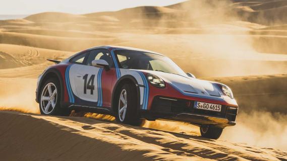 Porsche 911 Dakar met Martini-kleurstelling rijdend in de woestijn schuin voor