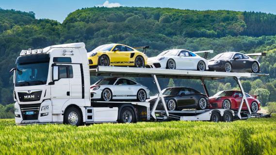 Porsche 911-collectie te koop met vrachtwagen en trailer vrachtwagen rijdend schuin voor groen