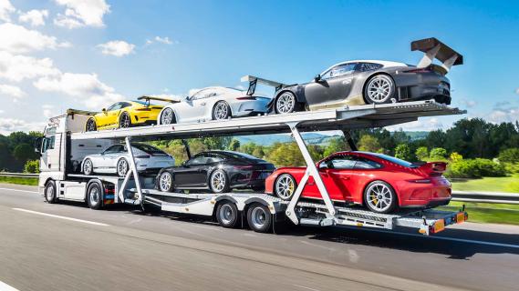 Porsche 911-collectie te koop met vrachtwagen en trailer vrachtwagen rijdend schuin achter snelweg
