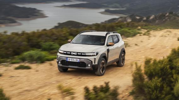 Dacia Duster Hybrid 140 Extreme grijs (2025) zijkant links schuin voor rijdend op zandpad op berg