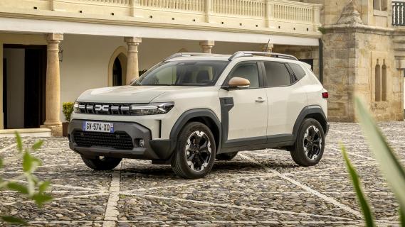 Dacia Duster Hybrid 140 Extreme grijs (2025) zijkant links voor schuin gebouw op binnenplein