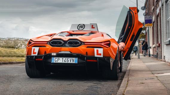 Lamborghini Revuelto lesauto oranje achterkant zij langs de weg