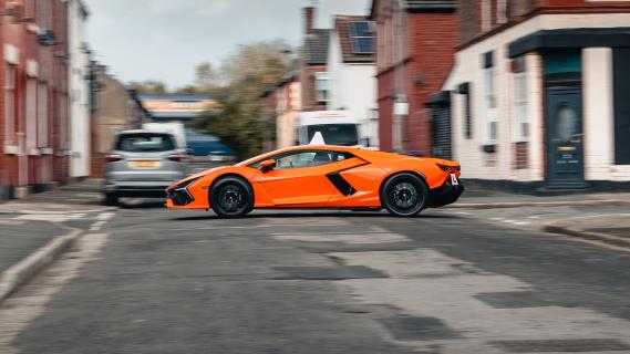 Lamborghini Revuelto lesauto oranje zijkant links rijdend door straat