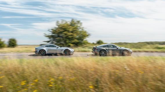 Aston Martin Vantage grijs & Porsche 911 Turbo S (992) groen zijkant rechts rijdend over weg boom gras