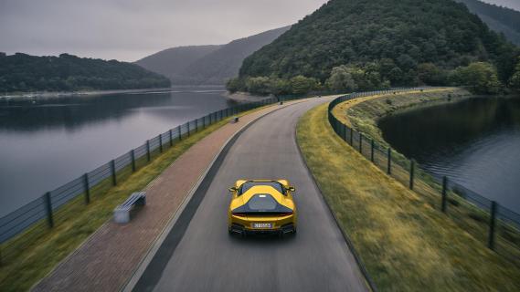 Ferrari 12Cilindri geel achterkant dijk hoog rijdend over weg