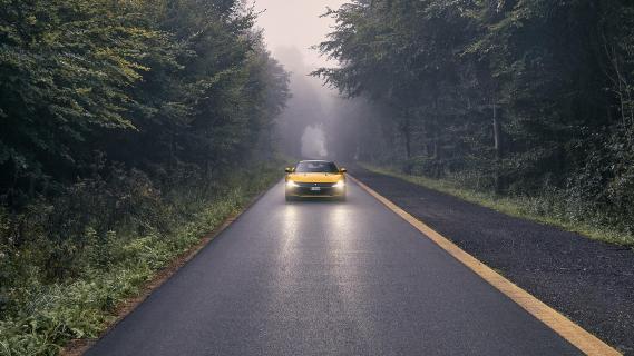 Ferrari 12Cilindri geel voorkant rijdend op natte weg bomen