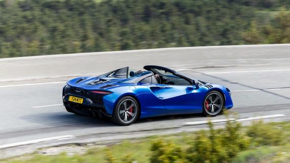 McLaren Artura Spider (2024) blauw zijkant achter schuin rechts rijdend op weg dak open