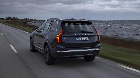 Volvo XC90 T8 blauw (2025) zijkant linksachter schuin rijdend over weg donkere wolken