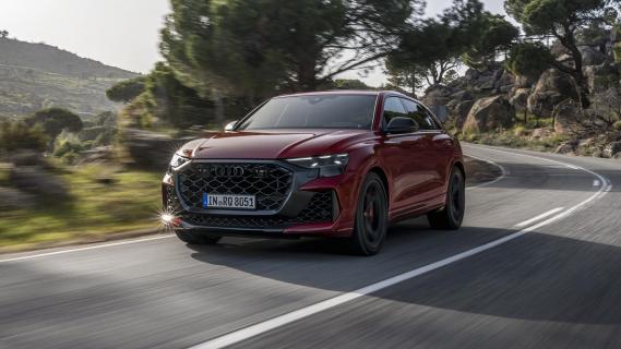 Audi RS Q8 Performance rood (2025) zijkant linksvoor schuin rijdend op weg bomen