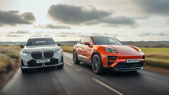 Porsche Macan Turbo Electric oranje (2025) en BMW X3 M50 (G45) grijs (2025) voorkant rijdend rechts schuin op weg wolken