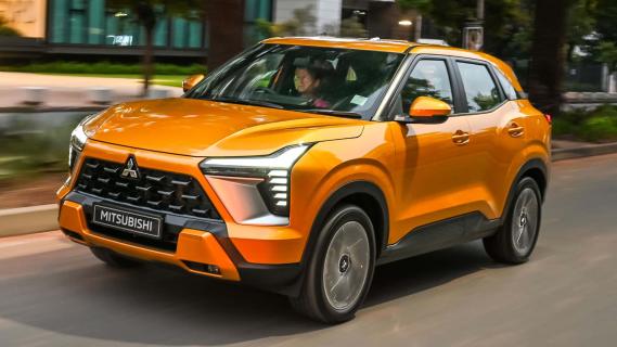 Mitsubishi Outlander Sport oranje (2025) zijkant links schuin rijdend op weg lichten aan