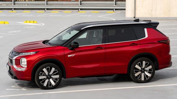 Mitsubishi Outlander PHEV rood (2025) zijkant links schuin voor parkeerplaats