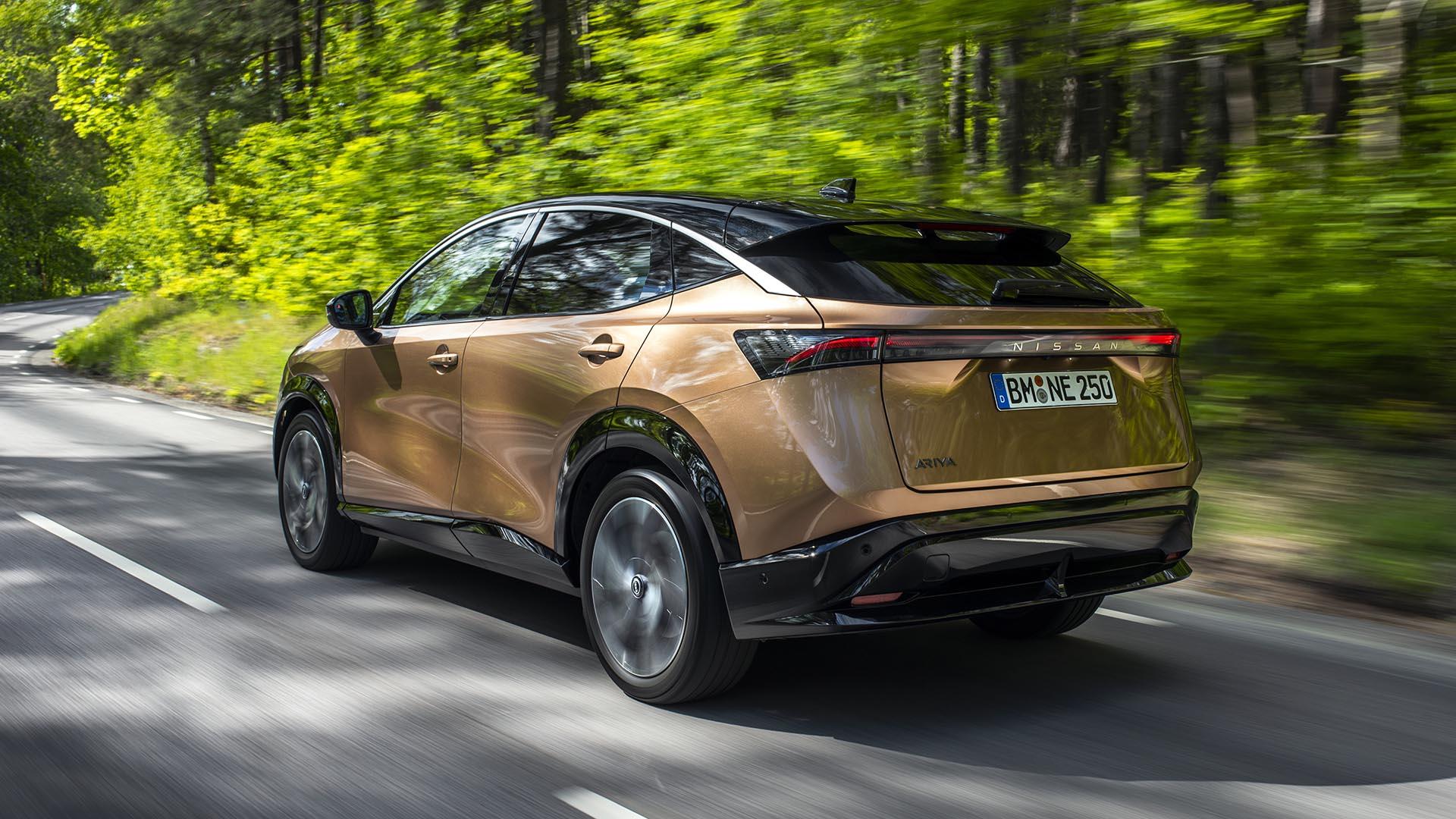 Nissan Ariya e-4orce Evolve Plus brons (2024) zijkant links achter rijdend overdag bomen struiken zonlicht