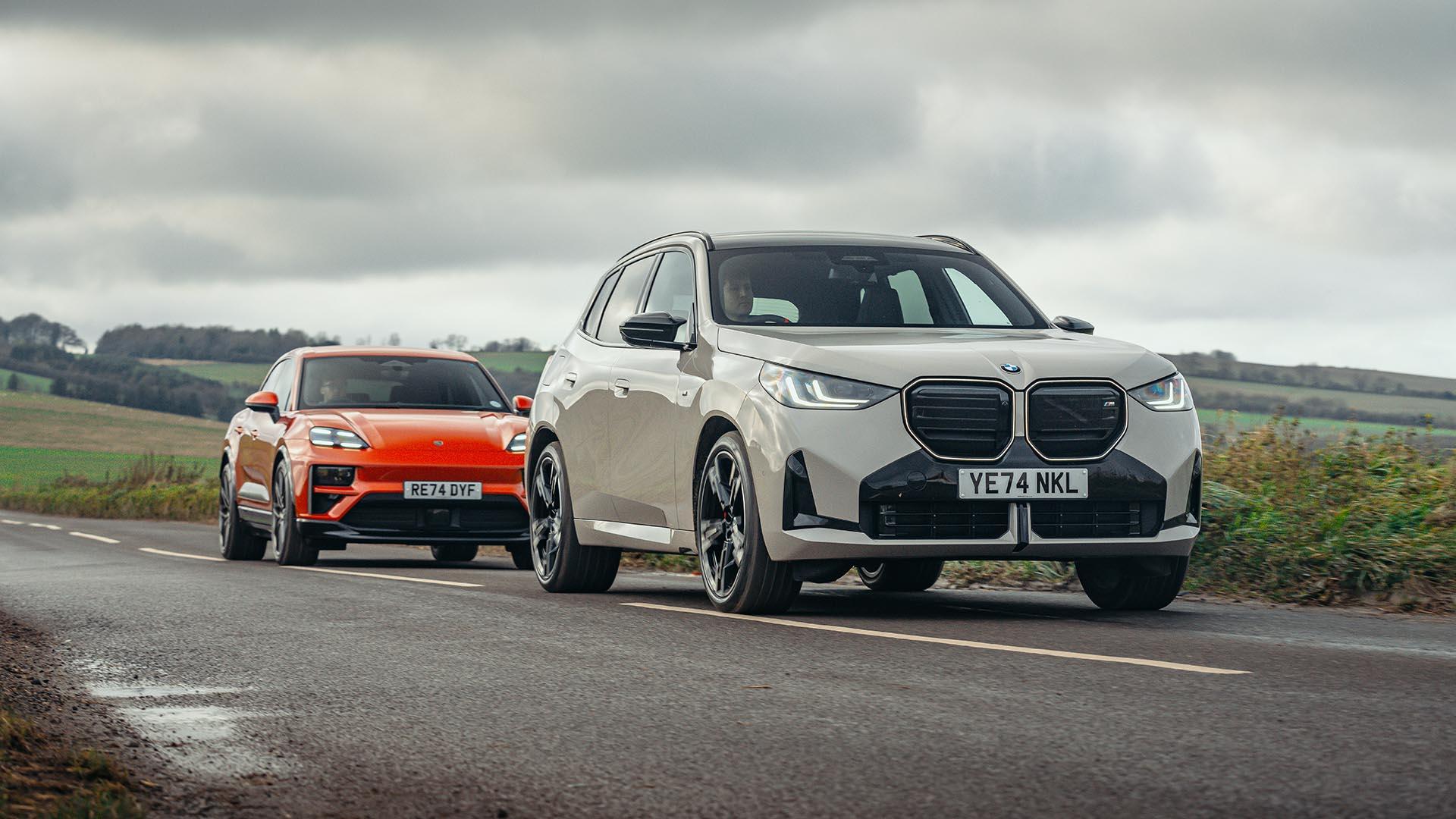 Porsche Macan Turbo Electric oranje (2025) en BMW X3 M50 (G45) grijs (2025) voorkant rijdend achter elkaar rechts schuin op weg wolken