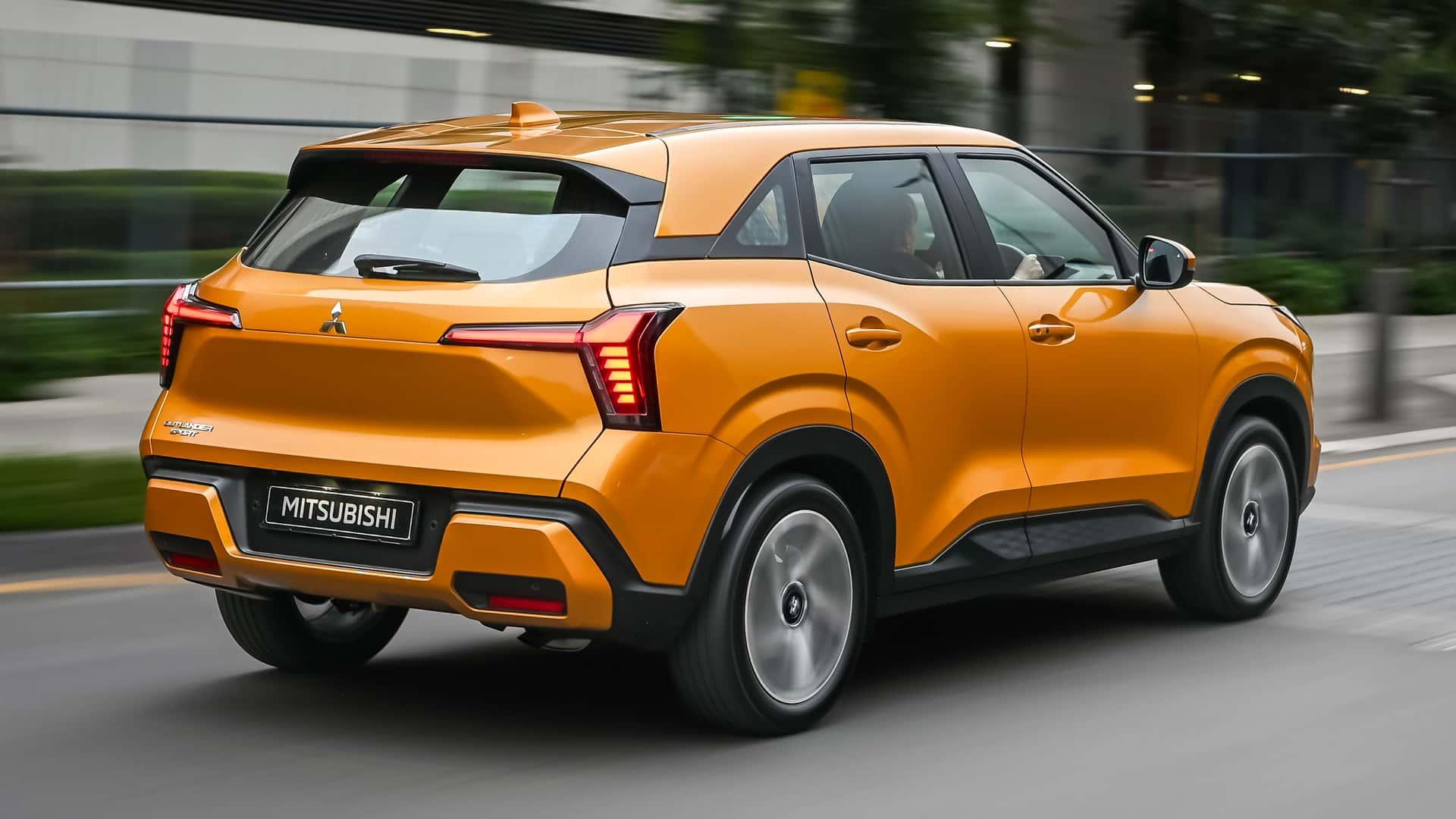 Mitsubishi Outlander Sport oranje (2025) zjikant rechts achter schuin rijdend op weg in stad lichten aan