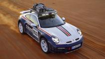 Porsche 911 Dakar Roughroads kleurstelling rijdend op een zandweg schuin voor van boven stof